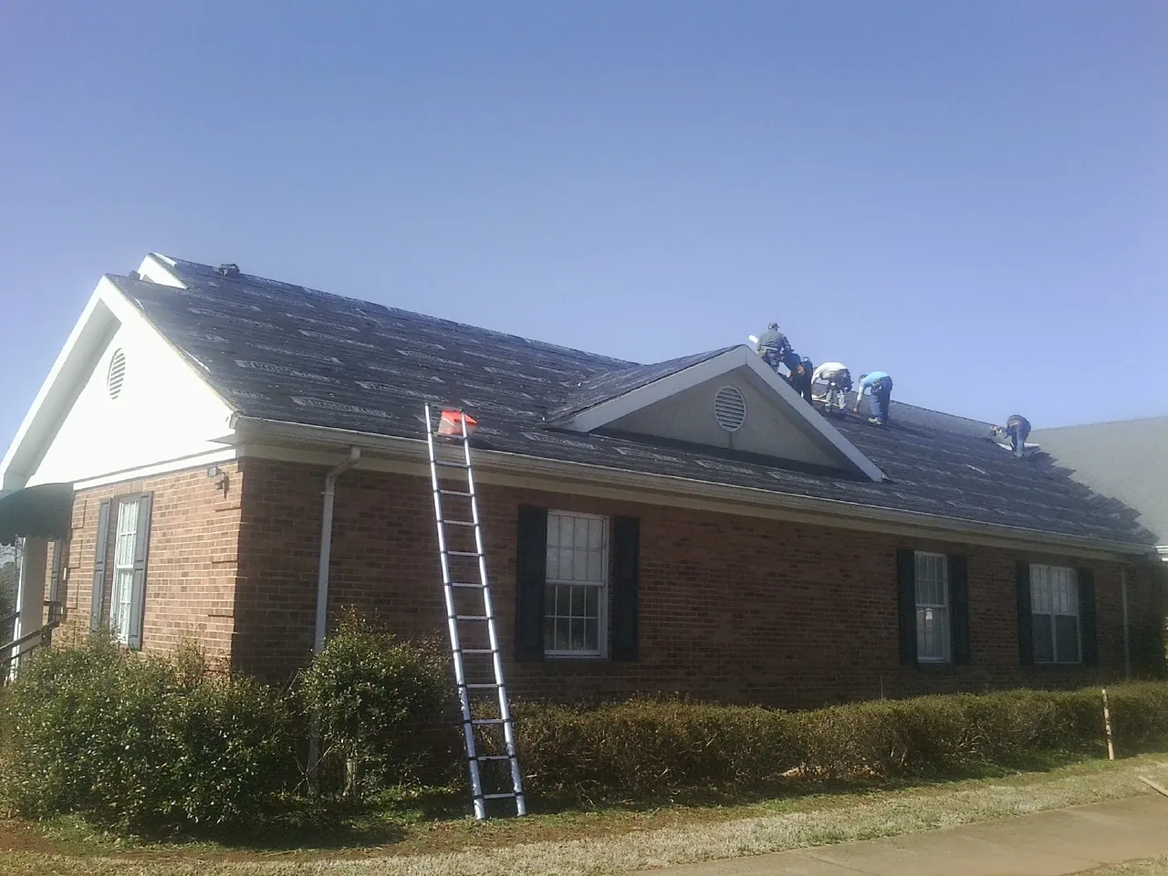 Crew tearing shingles off a brick ranch roof with a ladder set — Emergency Roof Repair work by our crew in Gretna