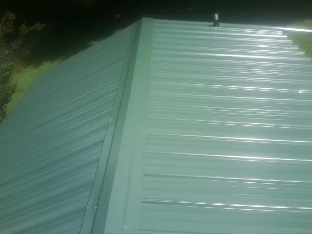 New green metal panels meeting at the ridge of a roof — Flat Roof Repair work by our crew in Gretna