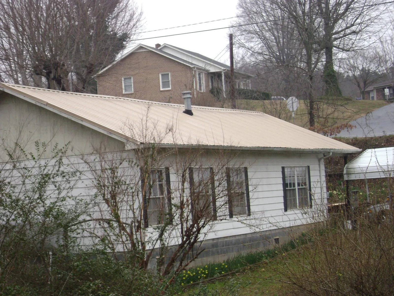 Tan metal roof on a white sided house set into a hillside — Commercial Roofing by Roofing Brothers in Gretna